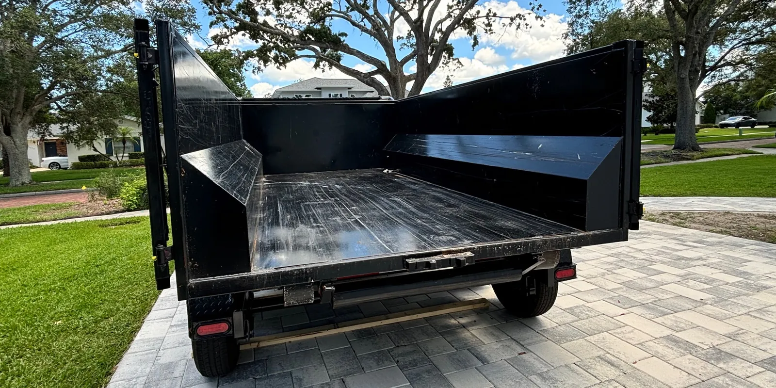 Empty Eco Haul dump trailer with its tailgate open on a paver driveway, ready to be loaded