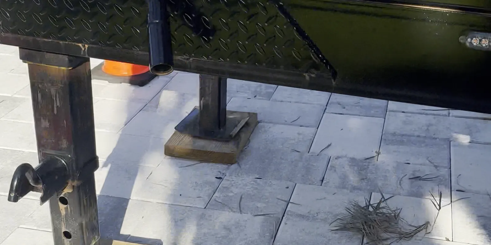 Trailer jack resting on a wooden block on a paver driveway