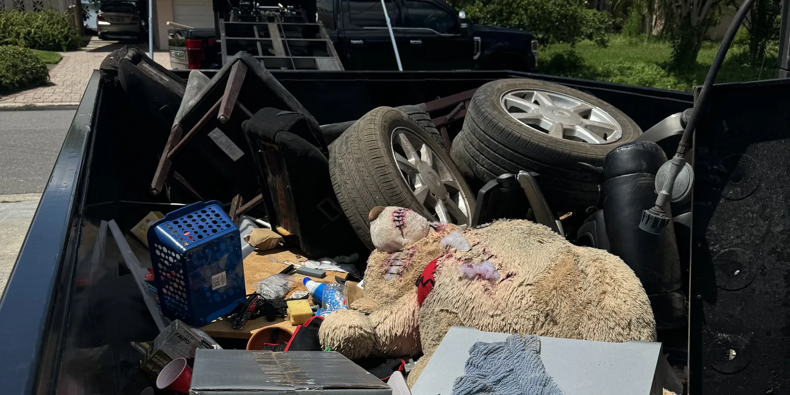 Dump trailer loaded with tires, boxes, a laundry basket and a large stuffed bear, seen from above