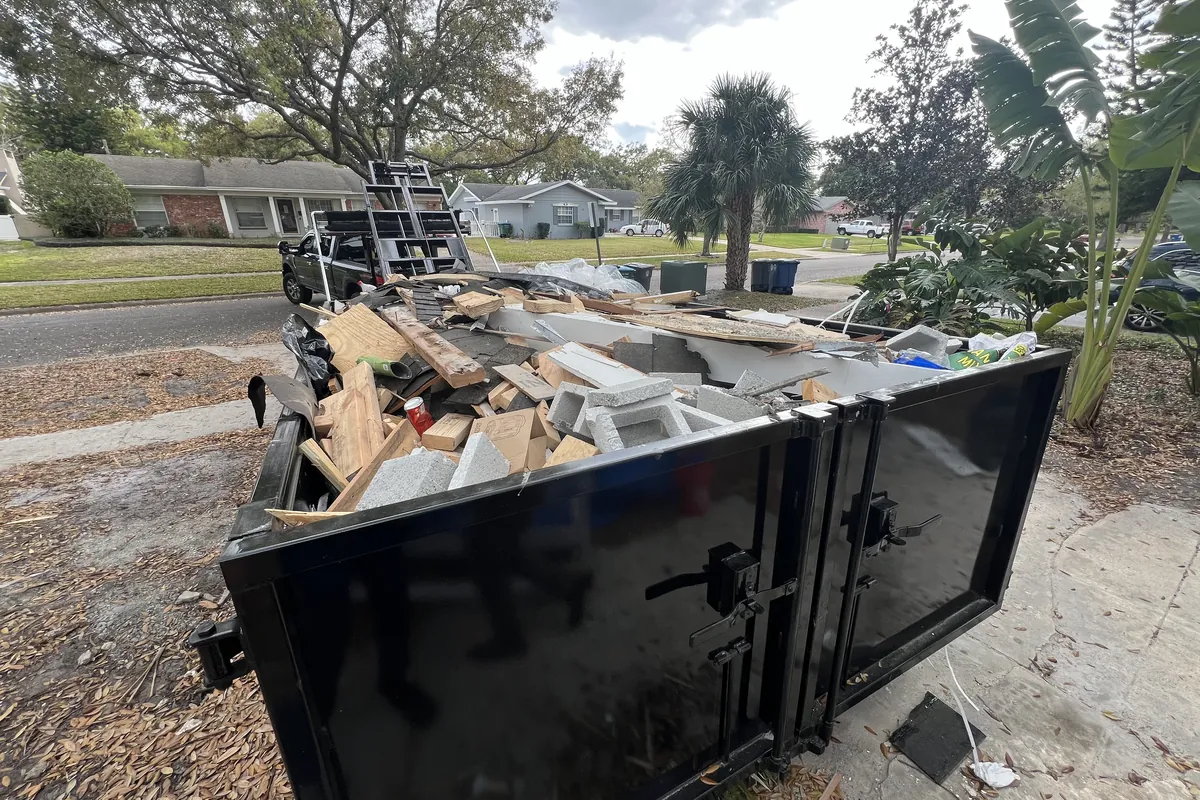 Eco Haul roll off container on a driveway, loaded with lumber, drywall and concrete block from a renovation