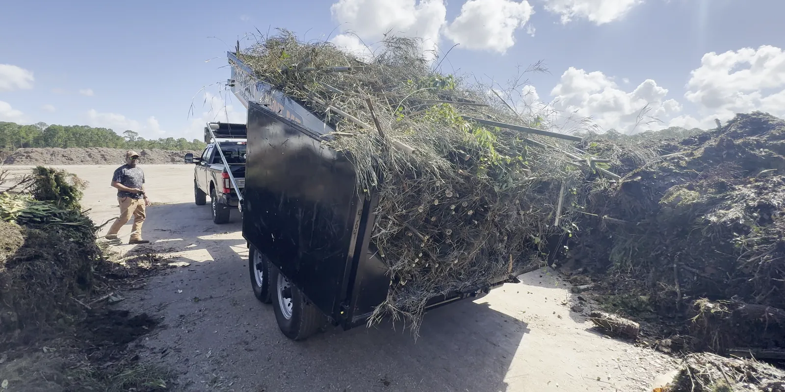 Eco Haul dump trailer loaded with branches and brush at the disposal yard, a crew member walking past the truck